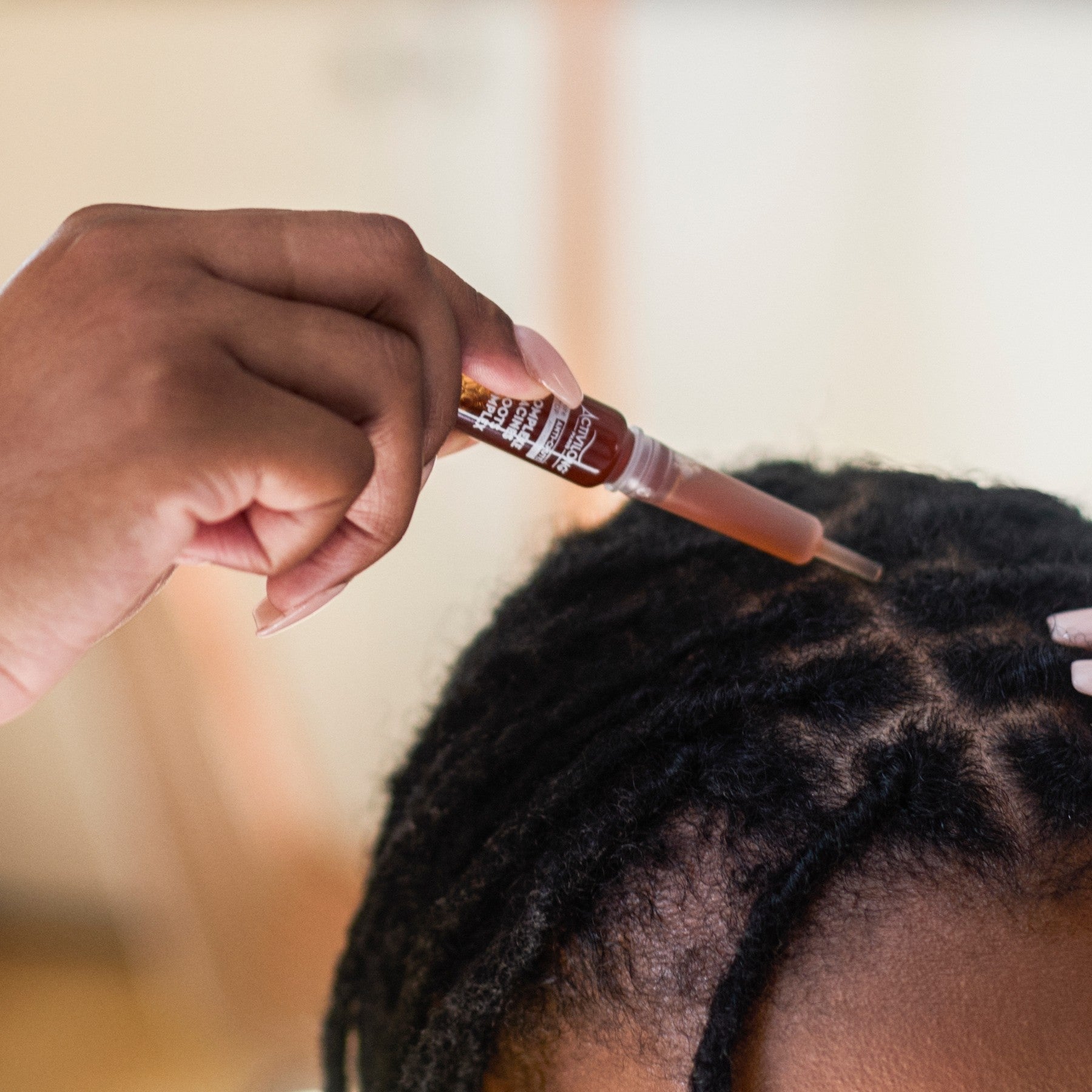 Person applying an ACTIVILONG ACTIGRO Complexe Racines 30ml Hair Serum to hair extensions using a small applicator.