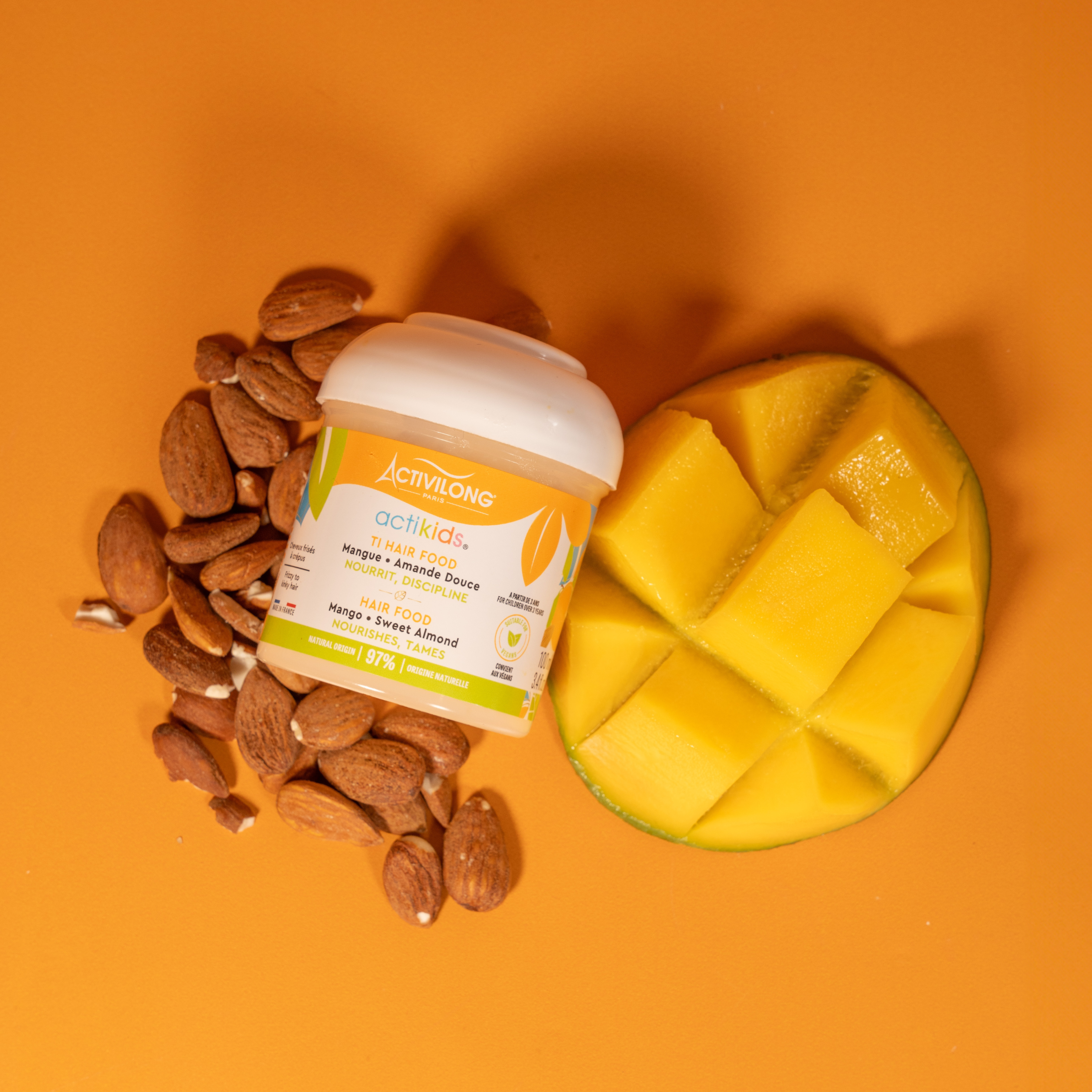 ACTIVILONG ACTIKIDS Ti-Hair Food 100ml by Afro Beauty Store with almonds and a sliced mango on an orange background