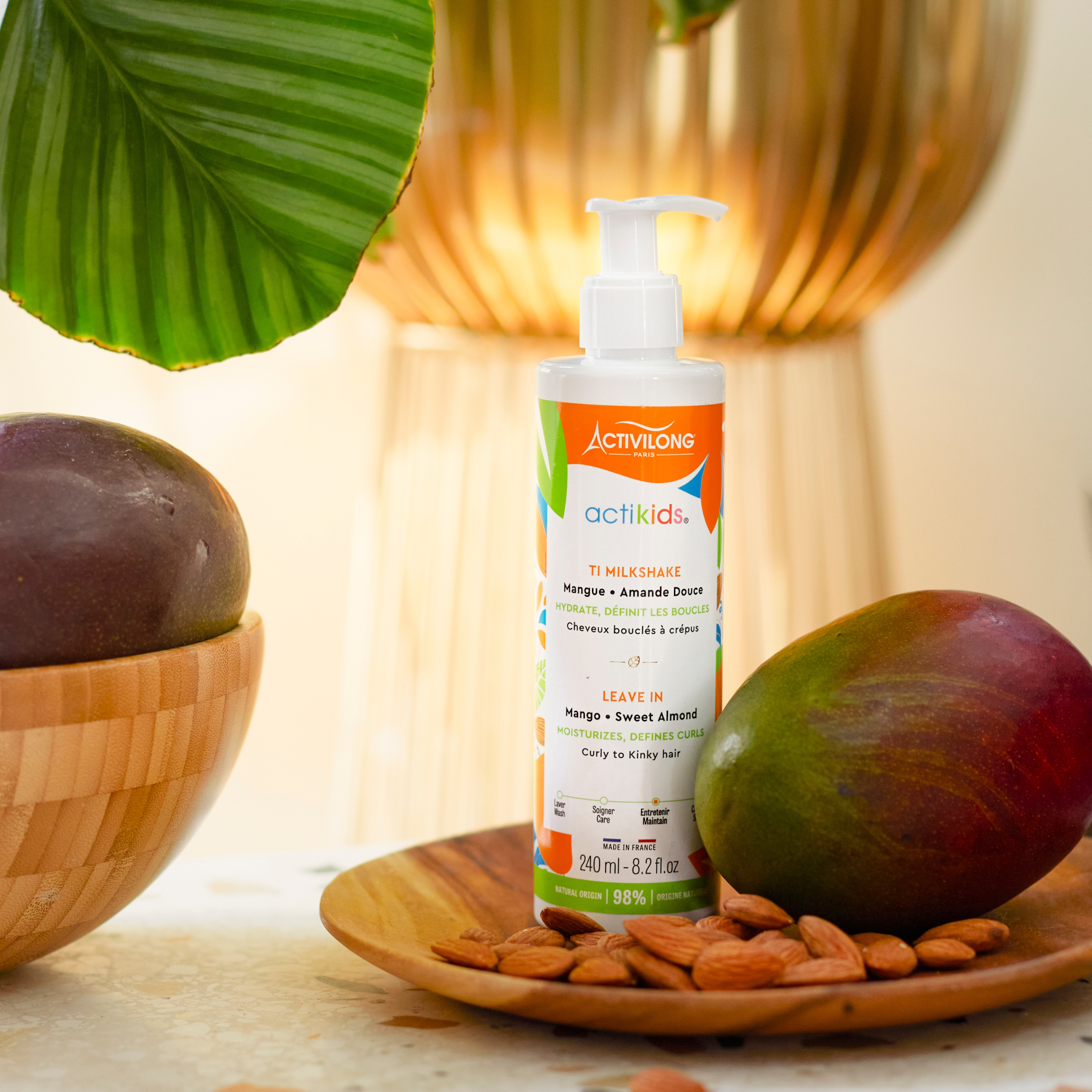 ACTIVILONG ACTIKIDS Ti Milkshake Leave-In 250ml bottle by Afro Beauty Store on a wooden plate with mangoes and almonds, surrounded by green leaves.