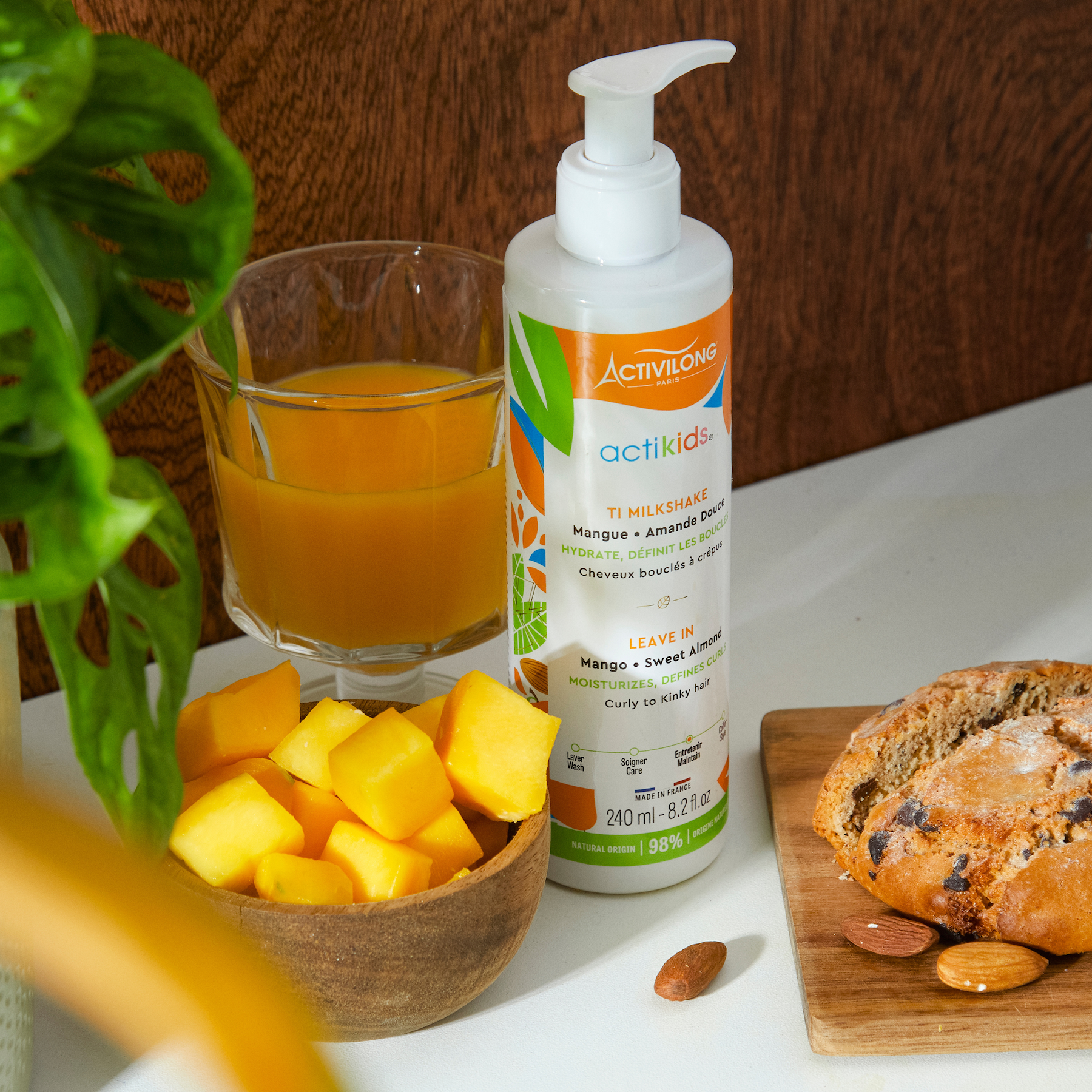 ACTIVILONG ACTIKIDS Ti Milkshake Leave-In 250ml bottle by Afro Beauty Store of termitaire with a glass of orange juice, bowl of mangoes, and bread on a white surface.