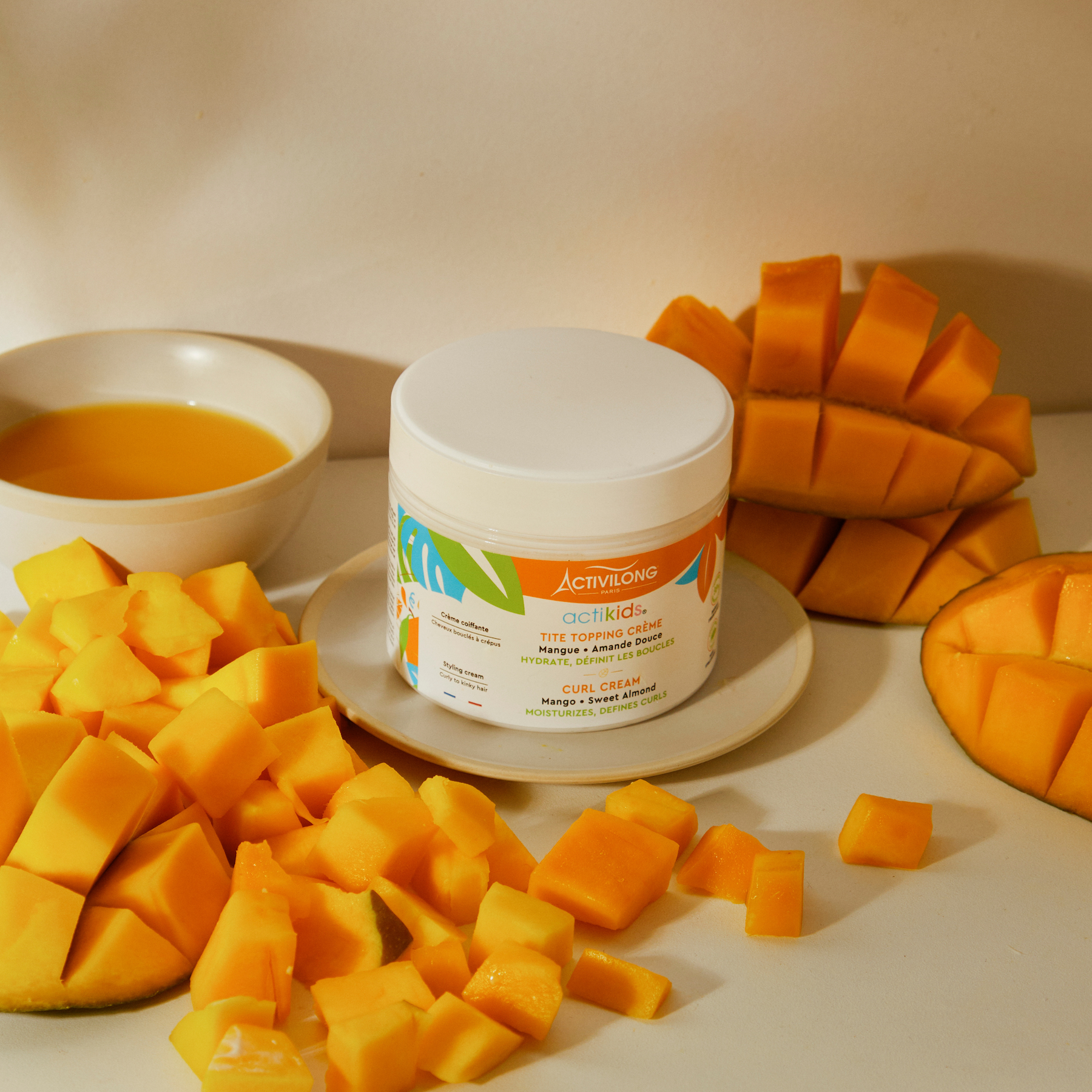 Jar of ACTIVILONG ACTIKIDS Tite Topping Crème 300ml surrounded by sliced mangoes on a white surface.