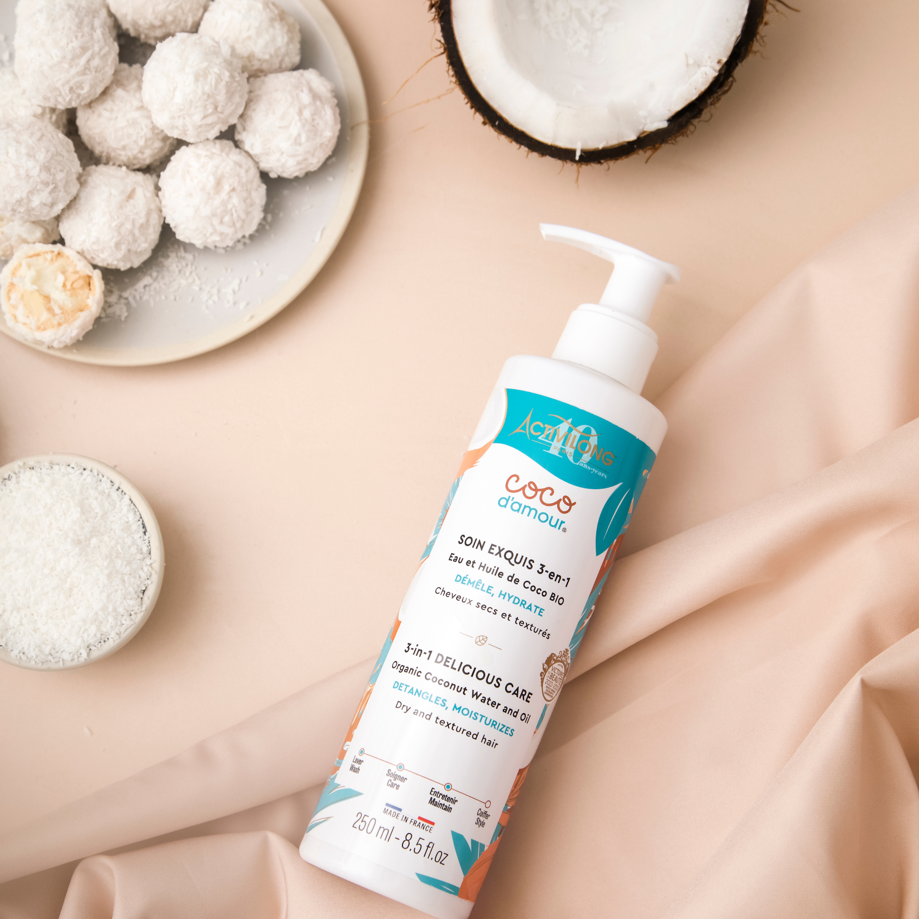 Bottle of ACTIVILONG COCO D’AMOUR Masque Soin Exquis 3-en-1 250ml by ABS France Wholesale on a beige fabric background with coconut and coconut balls.