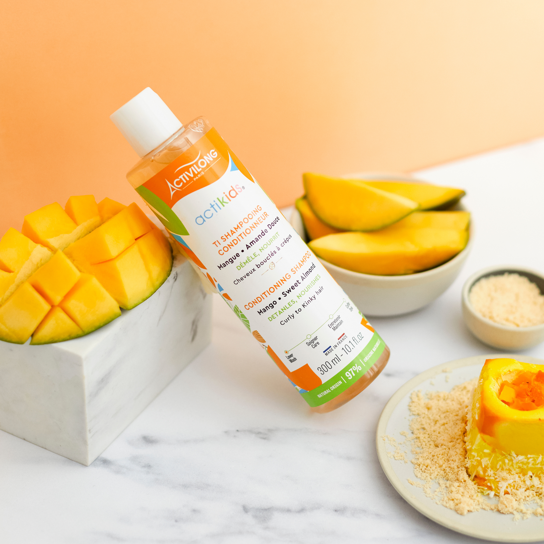 ACTIVILONG ACTIKIDS Ti-Shampooing Conditionneur 250ml bottle by Afro Beauty Store with mango slices and a smoothie on a marble surface.