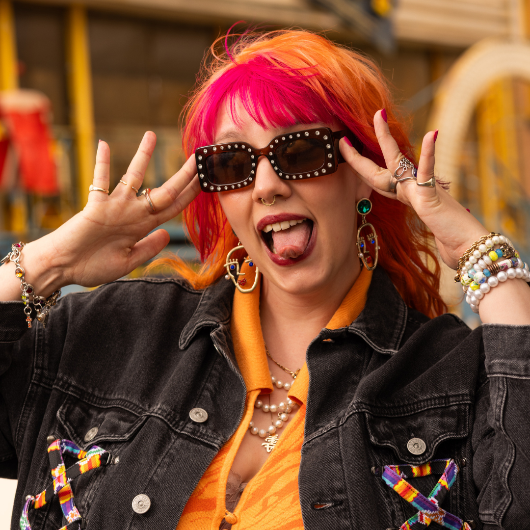 Crazy Color's Person with colorful hair and sunglasses making a peace sign, wearing an orange shirt and black jacket - Afro Beauty Store