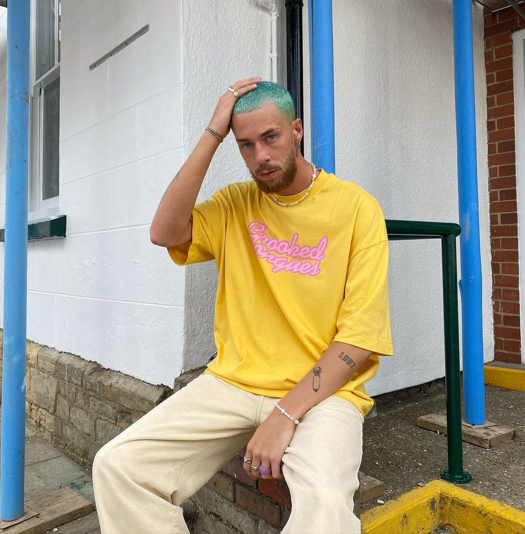 Crazy Color's Person wearing a yellow t-shirt with pink text, sitting on steps outdoors by Afro Beauty Store