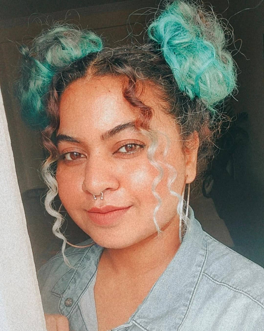 Crazy Color's Person with teal hair extensions styled in buns, wearing a denim shirt by Afro Beauty Store