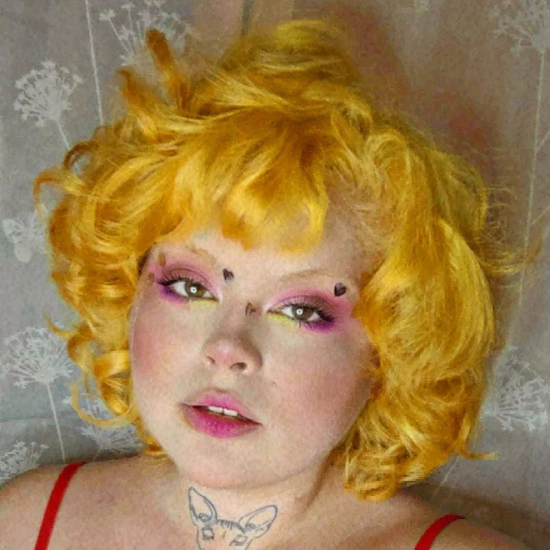 Crazy Color's Person with bright yellow hair and colorful makeup against a textured wall by Afro Beauty Store