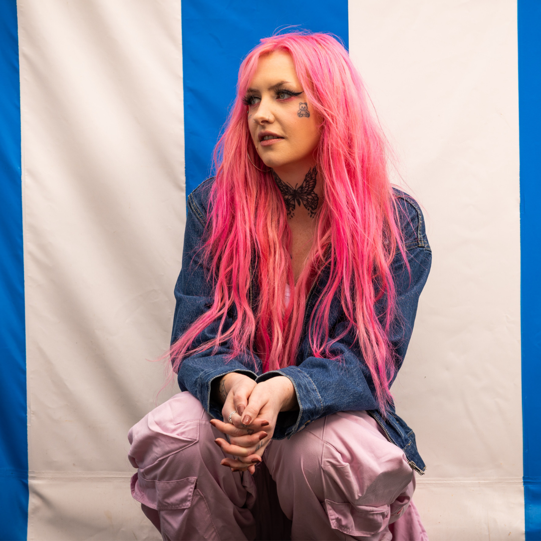 Crazy Color's Person with pink hair and denim jacket sitting against a striped background by Afro Beauty Store