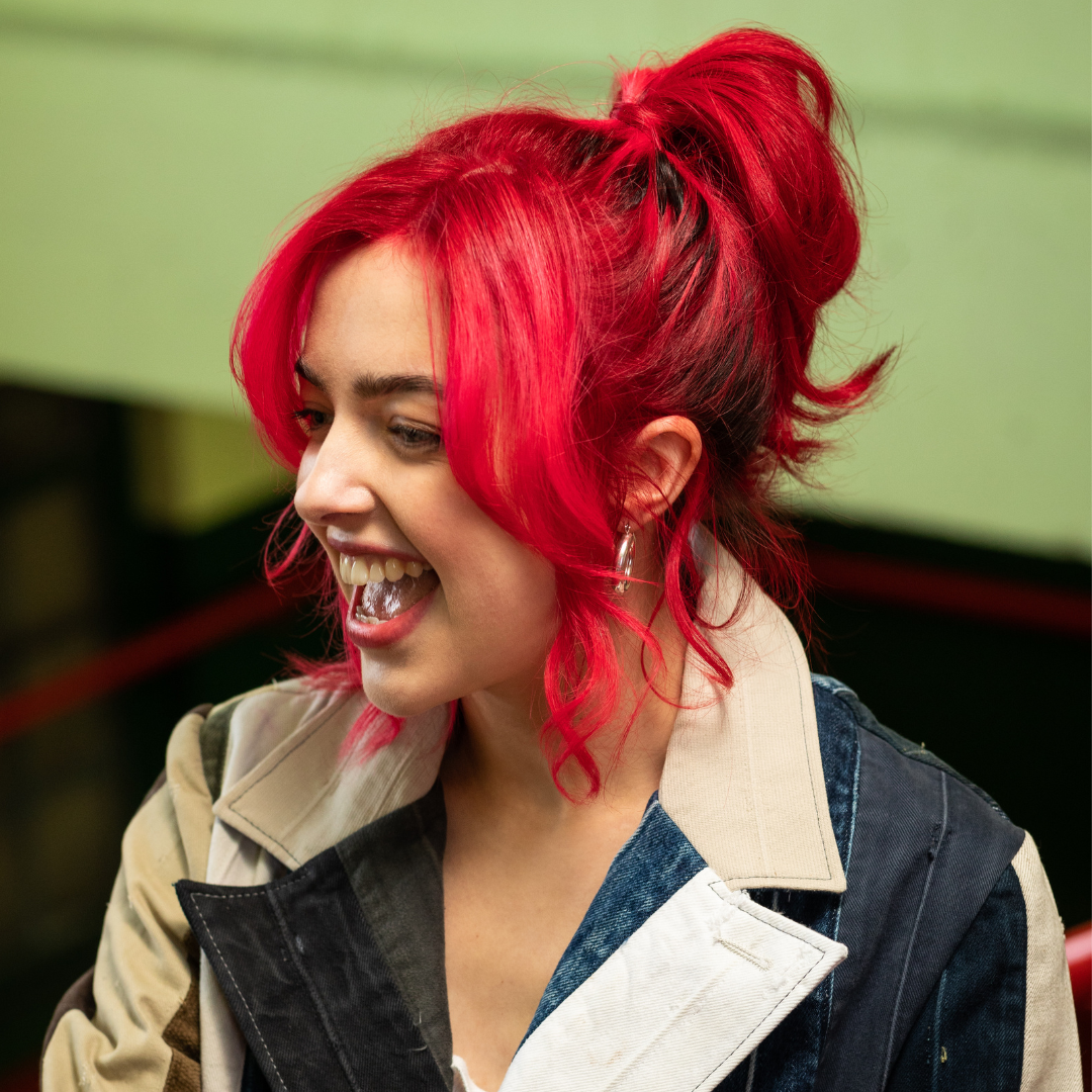 Crazy Color's person with red hair styled in a high ponytail, wearing a denim jacket with a beige collar by Afro Beauty Store