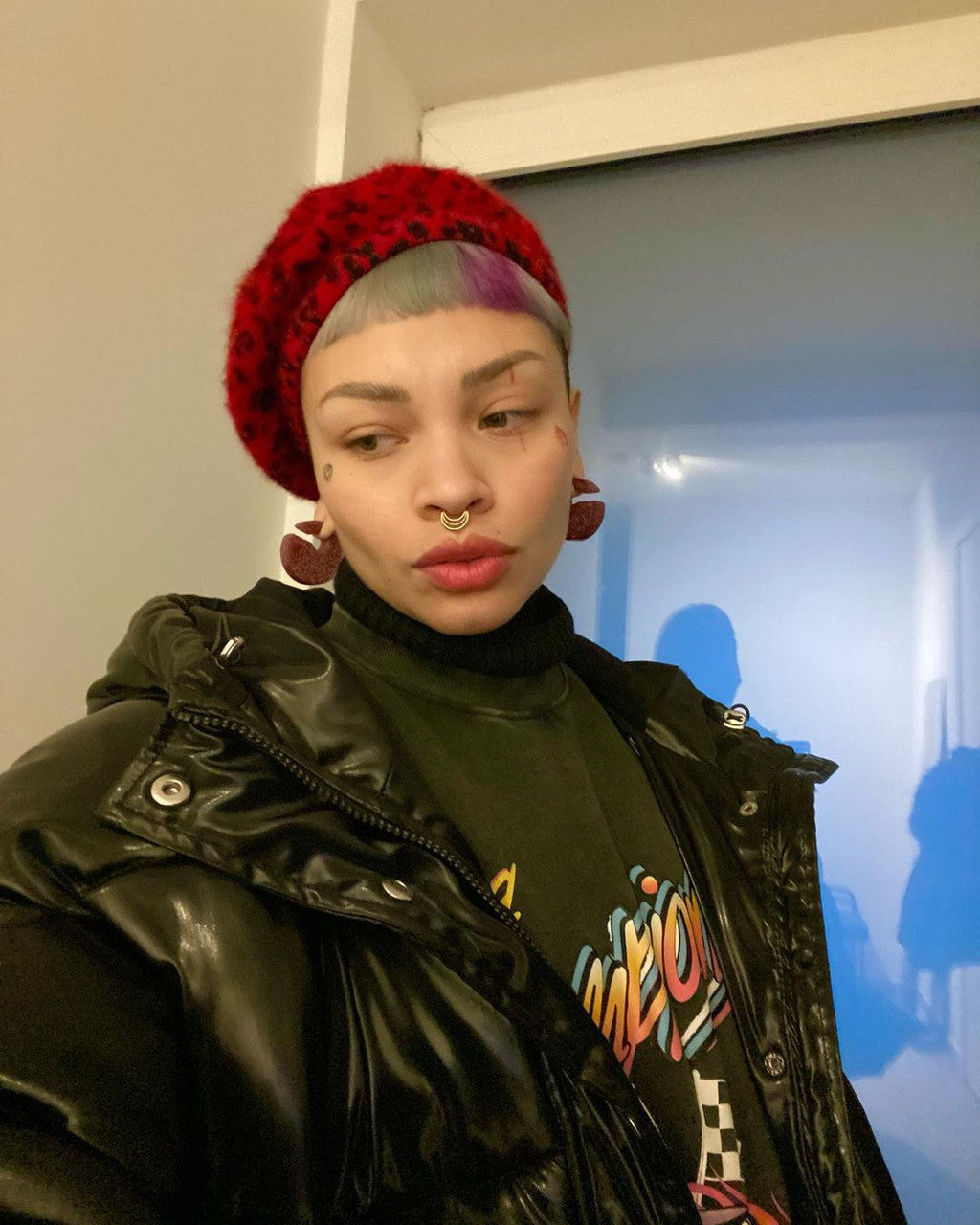 Crazy Color's Person wearing a red beanie and black jacket with colorful text, standing indoors by Afro Beauty Store