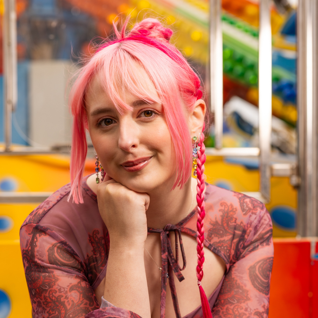 Crazy Color's person with pink hair and braids posing in front of a colorful background by Afro Beauty Store