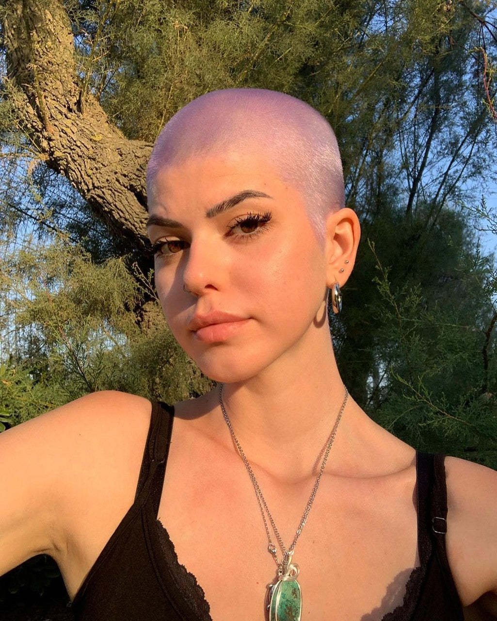 Crazy Color's person with a shaved head standing outdoors with trees in the background by Afro Beauty Store