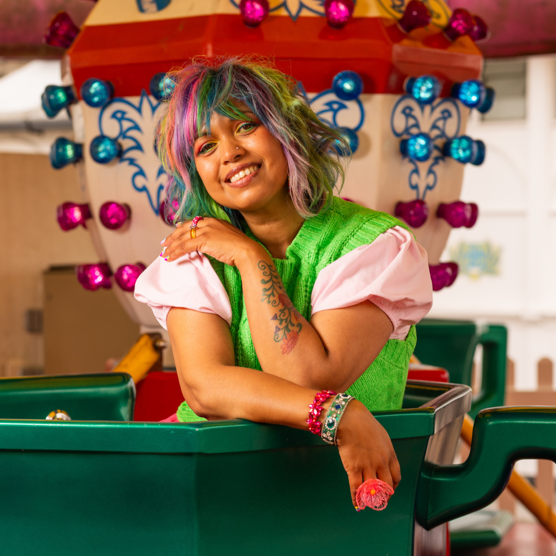 Crazy Color's Person with colorful hair and tattoos wearing a green dress in front of a festive background by Afro Beauty Store