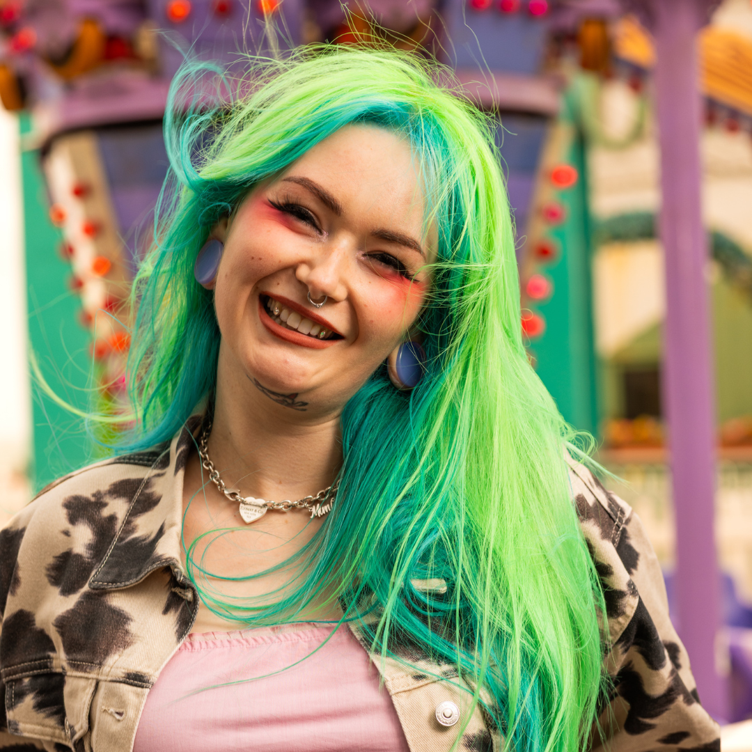 Crazy Color's Person with vibrant green and blue hair smiling in front of a colorful background by Afro Beauty Store