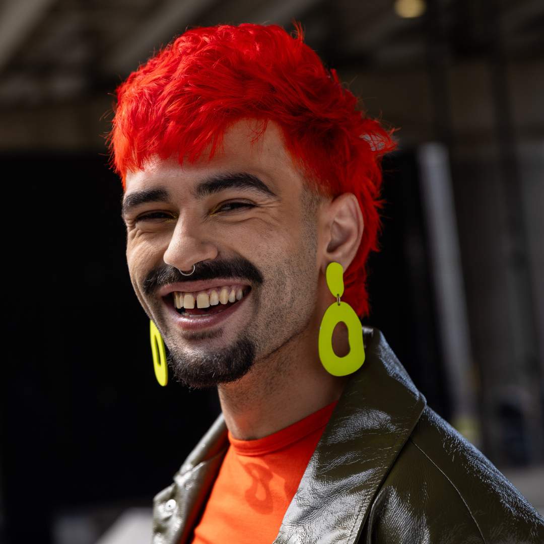 Crazy Color's Person with bright red hair and yellow earrings smiling outdoors by Afro Beauty Store