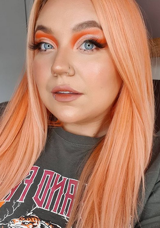 Crazy Color Person with peach hair and colorful makeup wearing a dark shirt with visible text by Afro Beauty Store