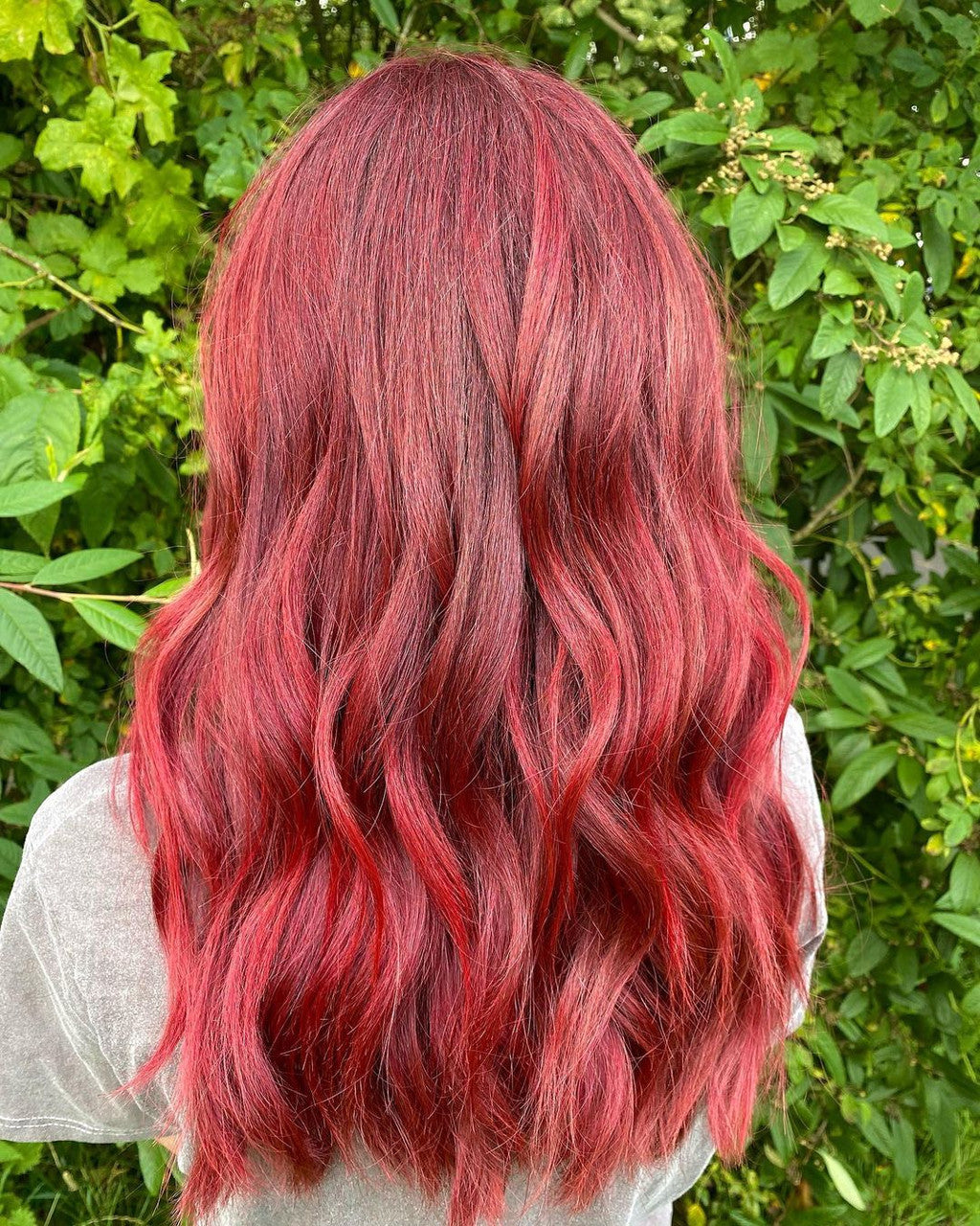 Crazy Color's Person with vibrant red hair standing in front of green foliage by Afro Beauty Store