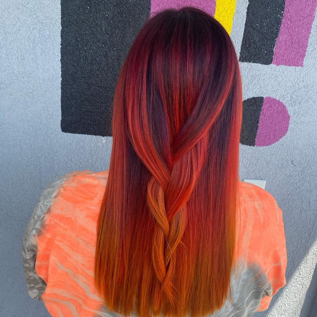 Crazy Color's Person with vibrant red and orange hair styled in a braid, wearing an orange top against a colorful abstract background by Afro Beauty Store