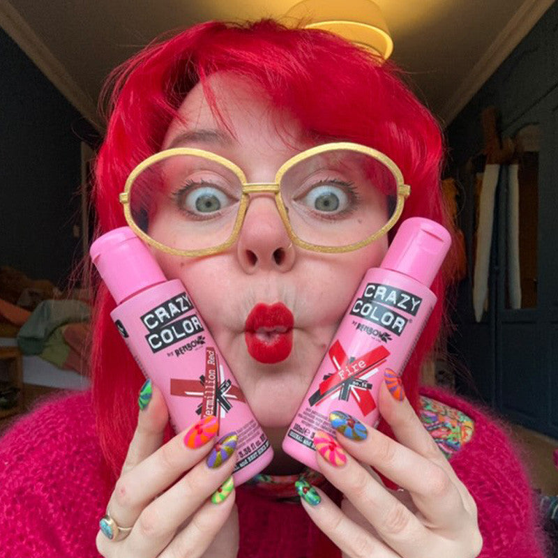 Person with bright red hair and colorful nails holding bottles of Crazy Color's vermillion red and fire hair dye by Afro Beauty Store