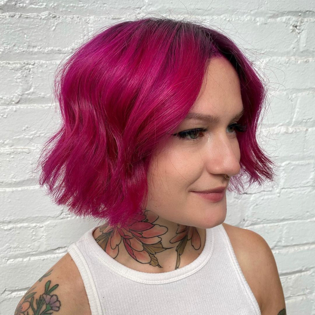 Crazy Color's Person with vibrant pink hair and tattoos against a white brick wall - Afro Beauty Store