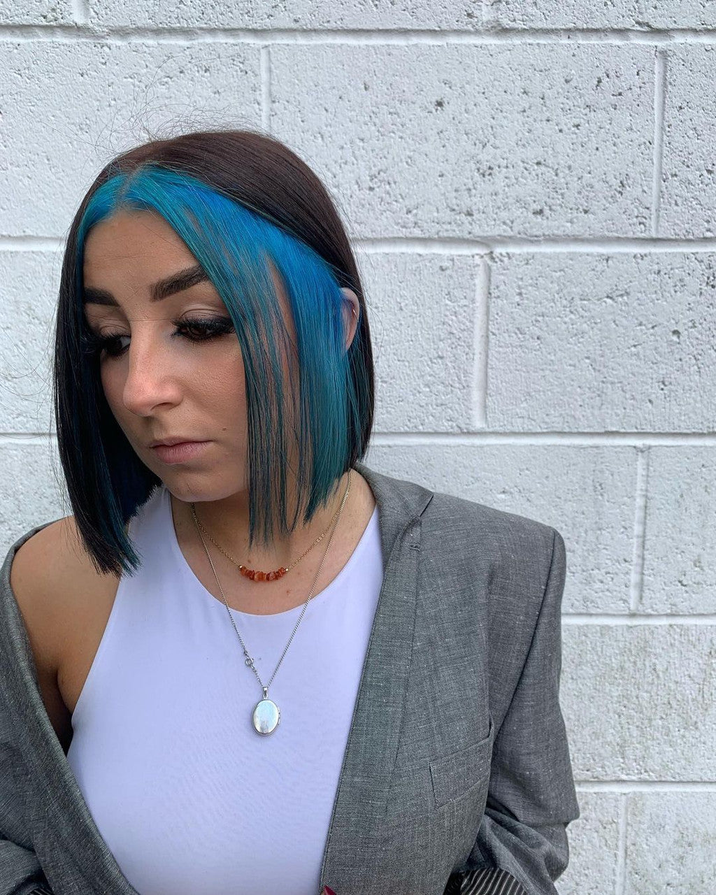 Crazy Color's person with blue hair and a gray blazer standing against a white brick wall by Afro Beauty Store