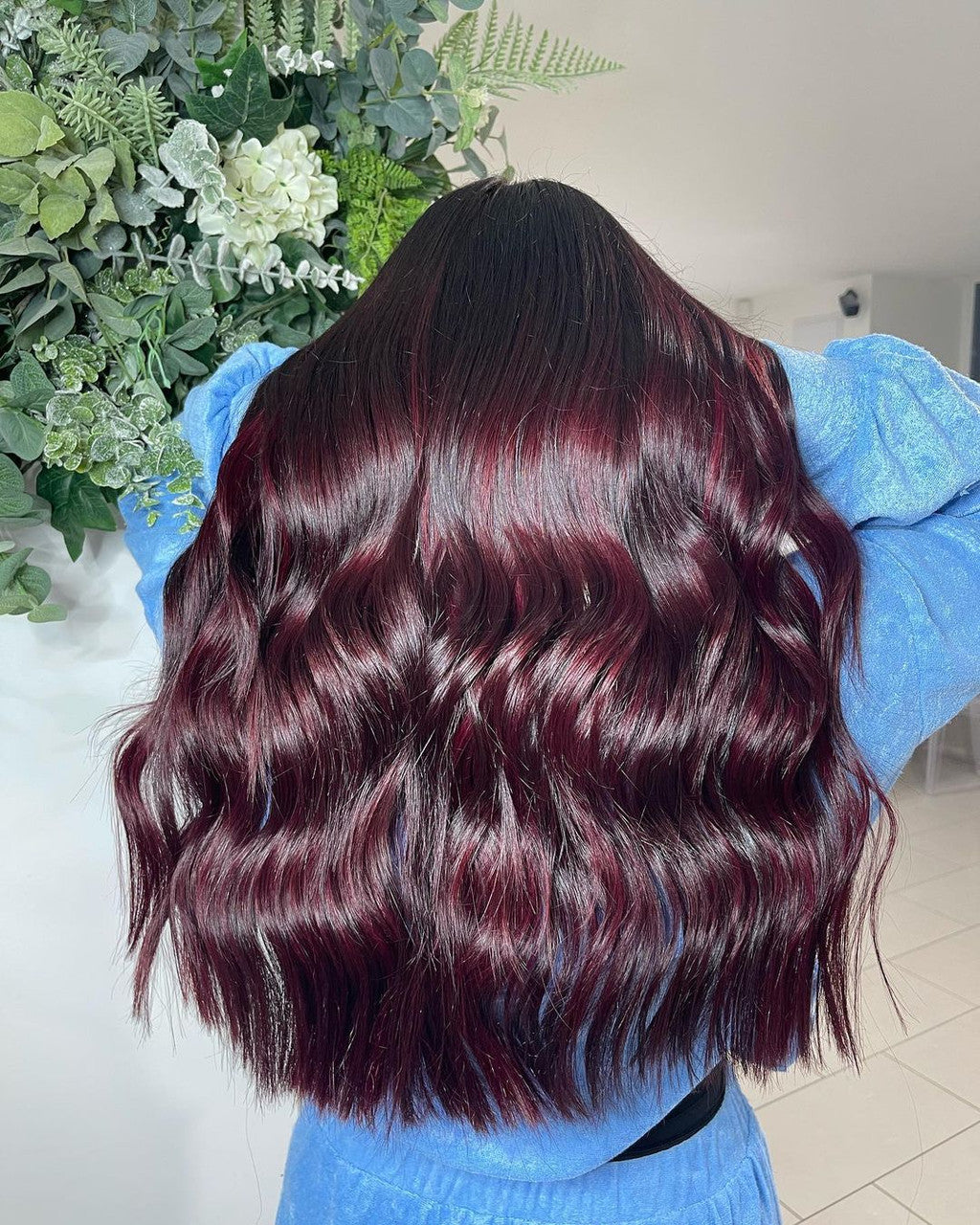 Crazy Color's Person with wavy, dark hair wearing a blue sweater in front of green plants by Afro Beauty Store
