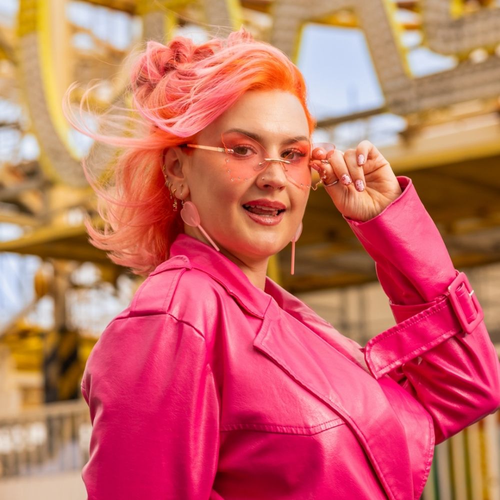 Crazy Color's Person with pink hair and pink jacket standing in front of a blurred background by Afro Beauty Store