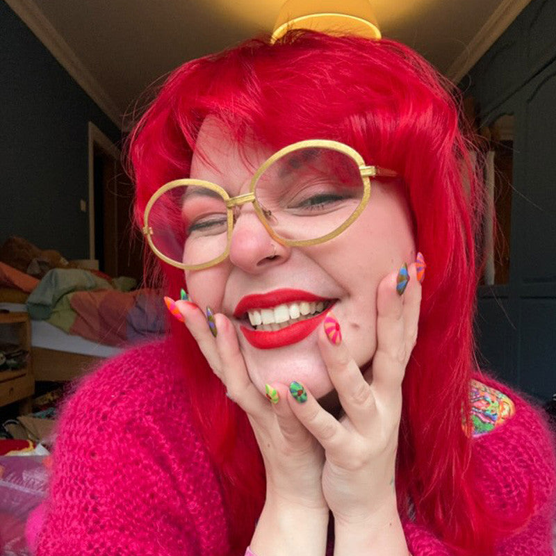 Person with red hair and pink sweater posing with hands on face in a casual setting - Afro Beauty Store