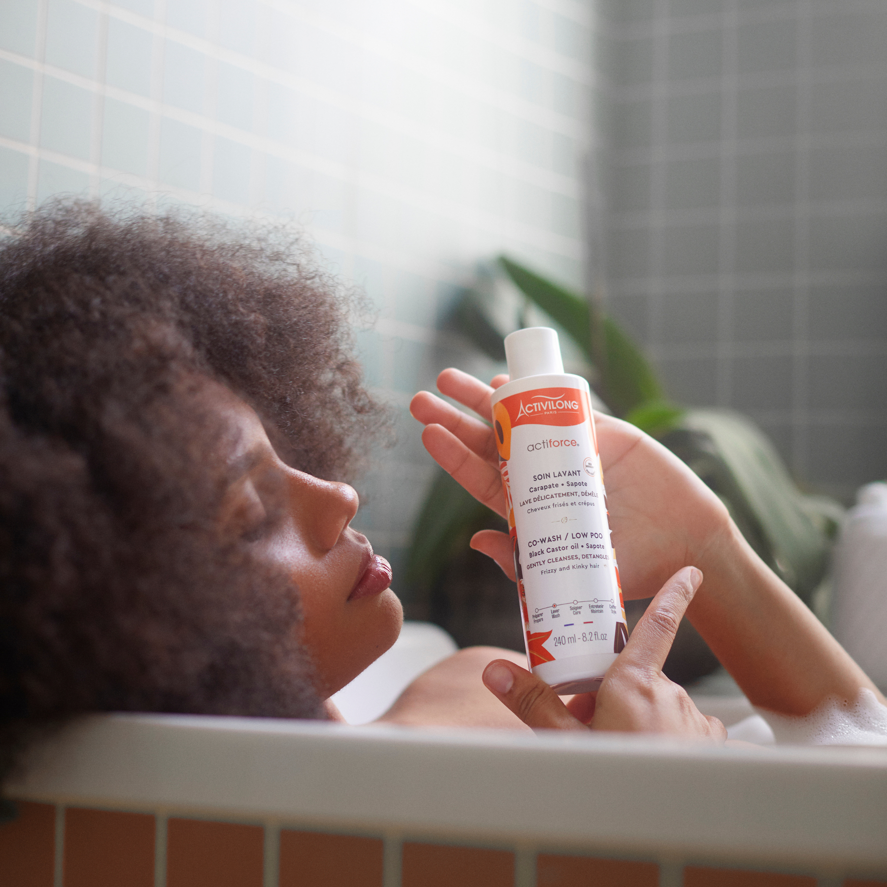 Person in a bathtub holding a Bottle of ACTIVILONG ACTIFORCE Co-wash 240ml by Afro Beauty Store