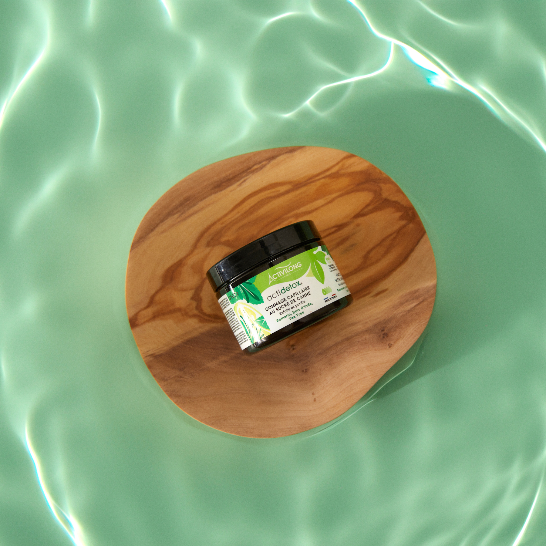 Jar of ACTIVILONG ACTIDETOX Gommage Capillaire 150ml by Afro Beauty Store on a wooden disc over green water