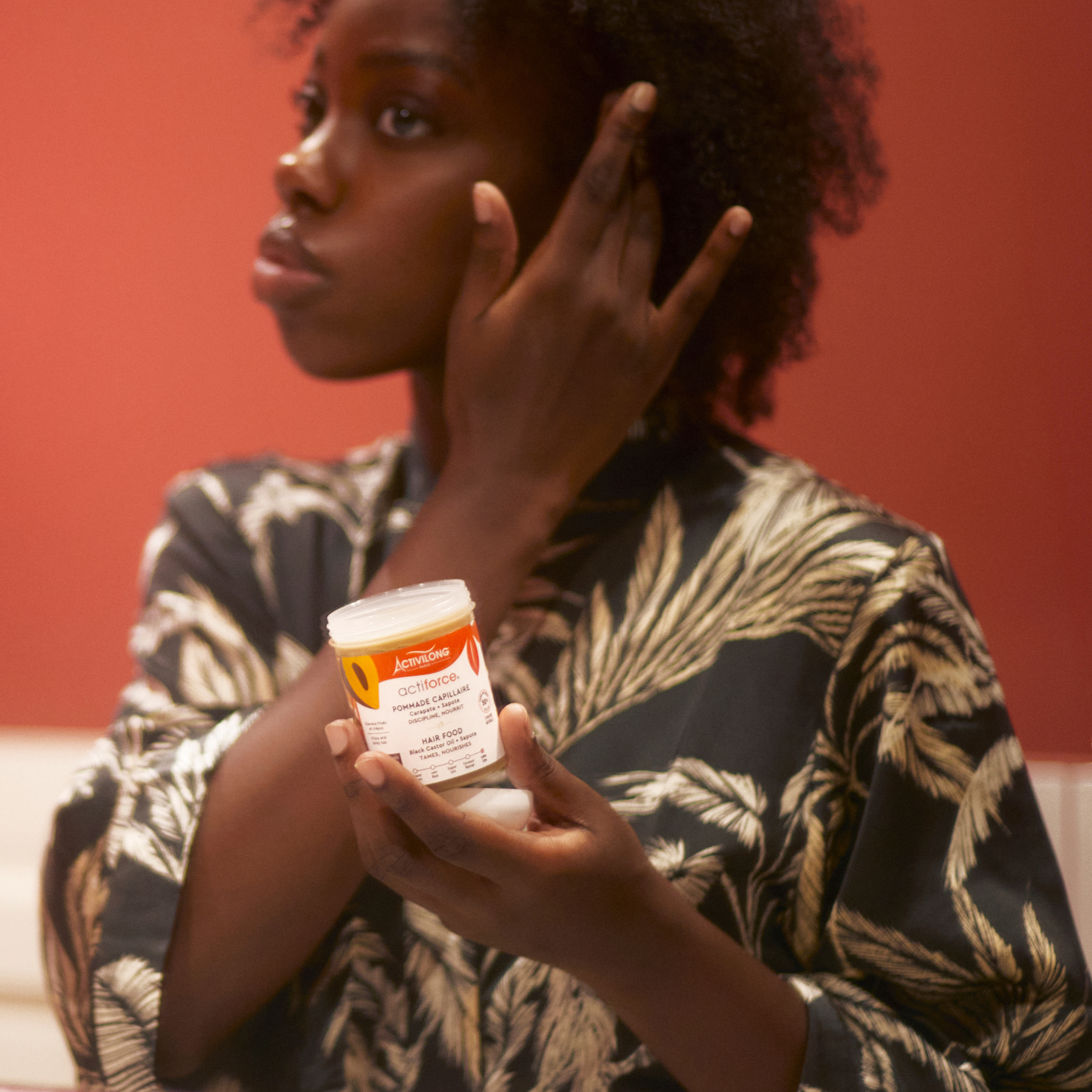 Woman holding an ACTIVILONG ACTIFORCE Pommade Fortifiante 100ml container by Afro Beauty Store with a red background