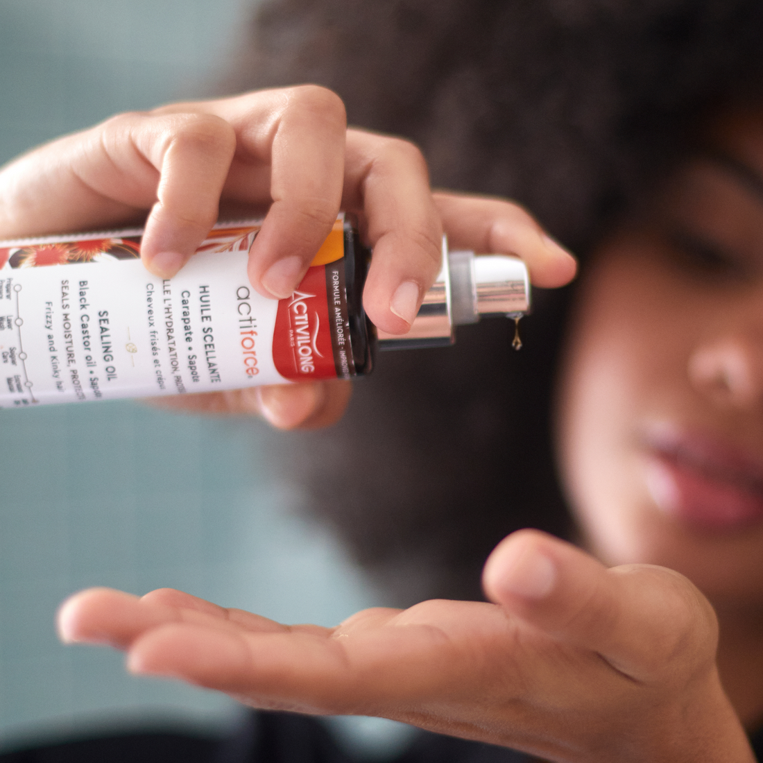 Person applying an ACTIVILONG ACTIFORCE Huile Scellante 125ml bottle by Afro Beauty Store to their palm with a blurred background