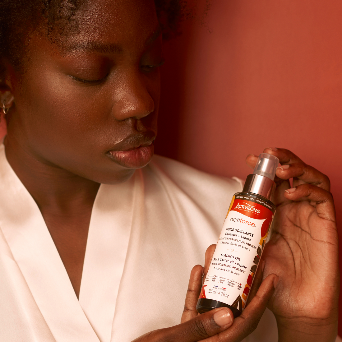Woman holding an ACTIVILONG ACTIFORCE Huile Scellante 125ml bottle by Afro Beauty Store with a red background