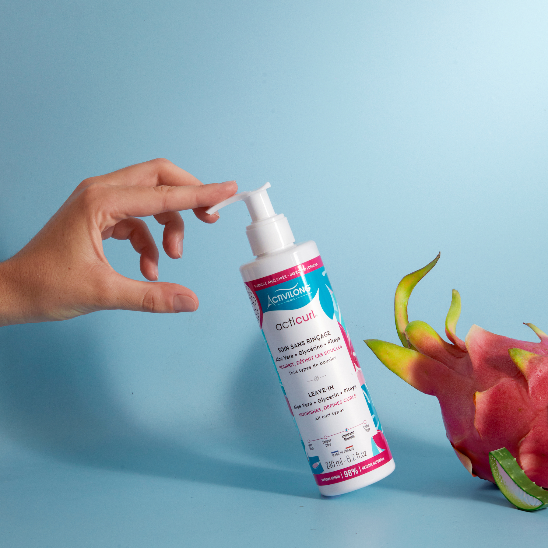 Hand holding a bottle of ACTIVILONG ACTICURL Leave-In 240ml by Afro Beauty Store with a dragon fruit on a blue background
