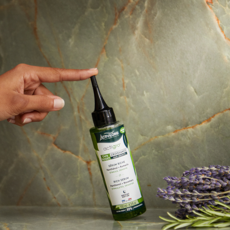 Hand holding a bottle of ACTIVILONG ACTIGRO Sérum Riche 130 ml bottle by Afro Beauty Store with lavender flowers on a marble background