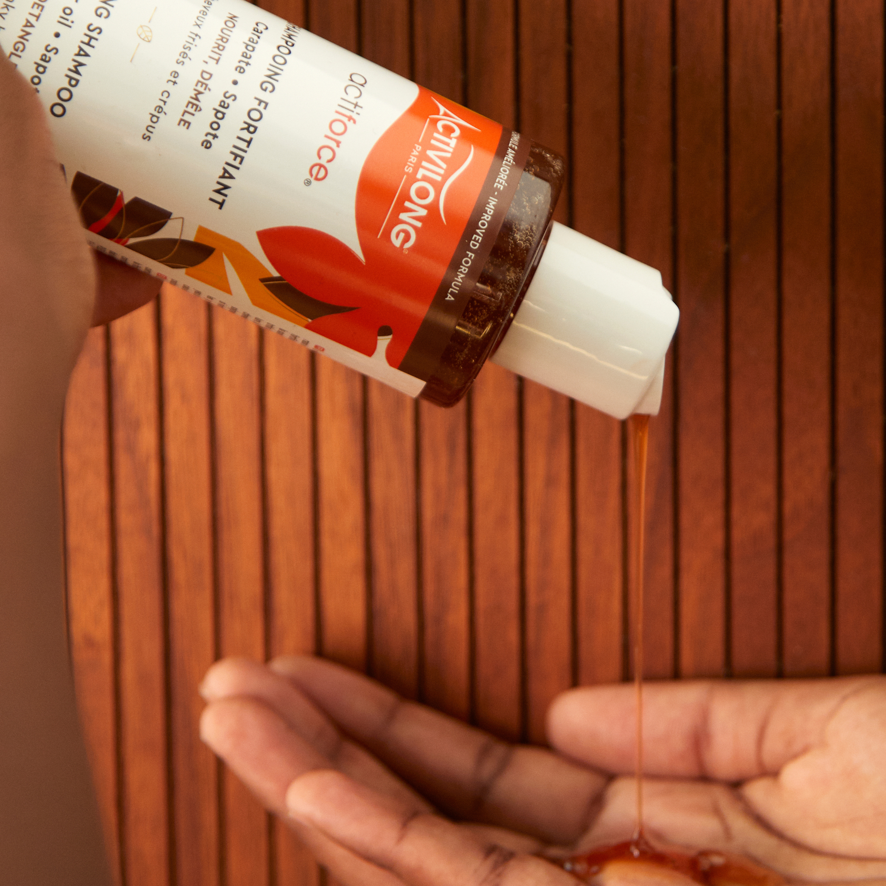Person pouring a liquid from an ACTIVILONG ACTIFORCE Fortifiant Shampoing 250ml bottle by Afro Beauty Store into their hand against a wooden background.