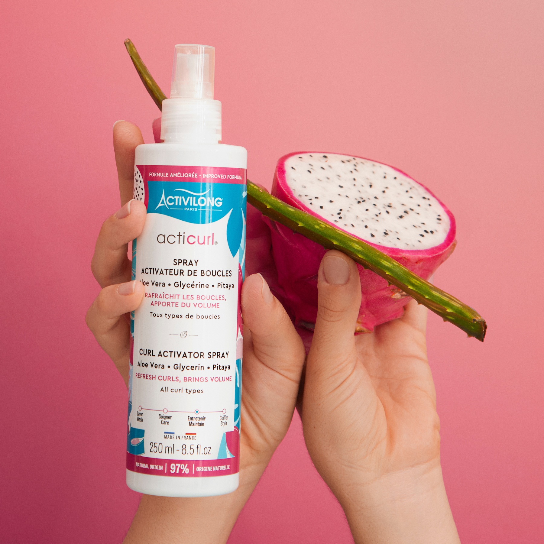 Hand holding a Bottle of ACTIVILONG ACTICURL Spray Activateur 250ml by Afro Beauty Store next to a dragon fruit and aloe vera against a pink background