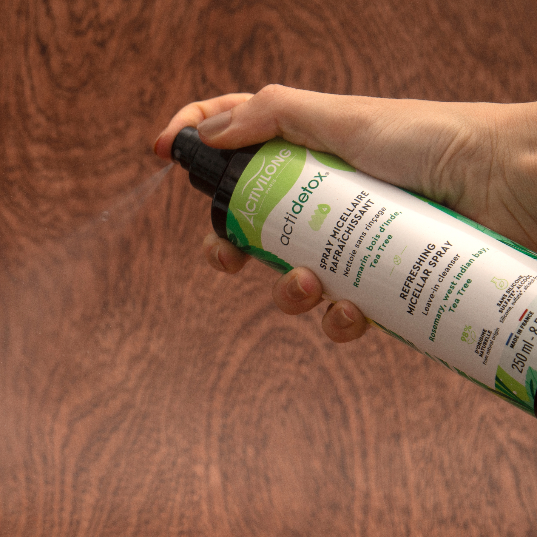 Hand holding a bottle of ACTIVILONG ACTIDETOX Spray Micellaire Rafraîchissant 250ml by Afro Beauty Store against a wooden background