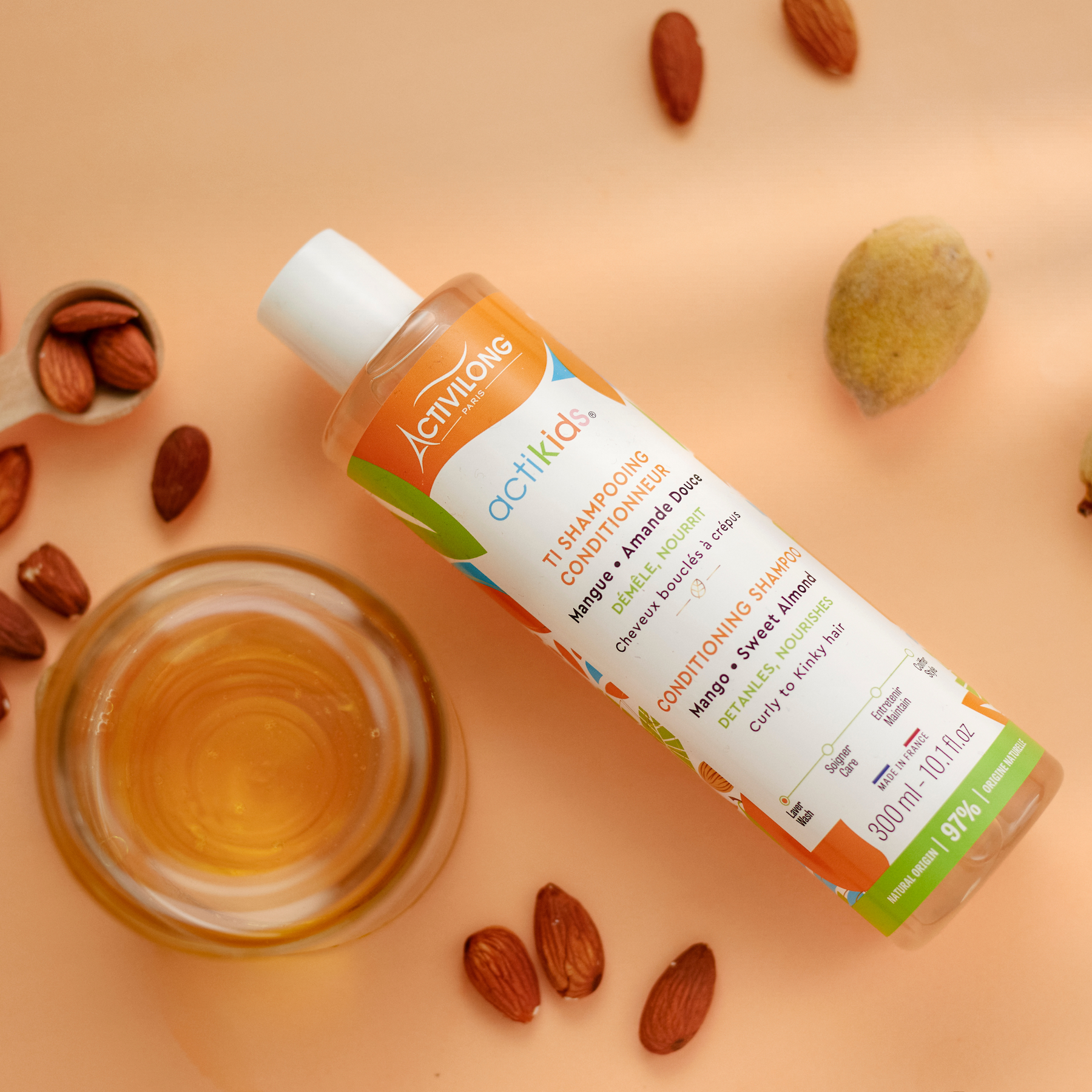 ACTIVILONG ACTIKIDS Ti-Shampooing Conditionneur 250ml bottle by Afro Beauty Store on a peach background with almonds and a small bowl of oil.